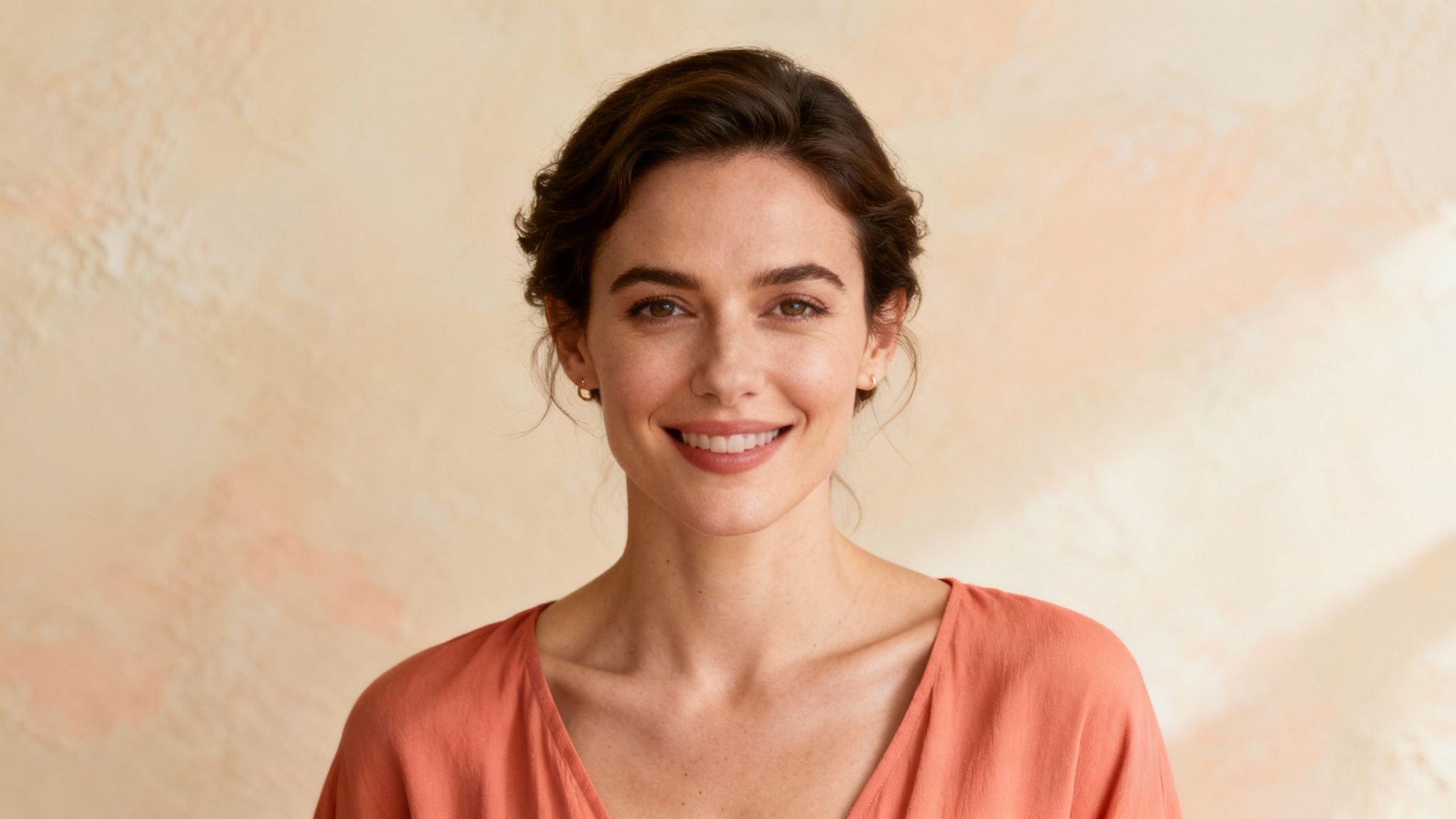Smiling woman wearing coral peach colored top against neutral beige background in studio portrait