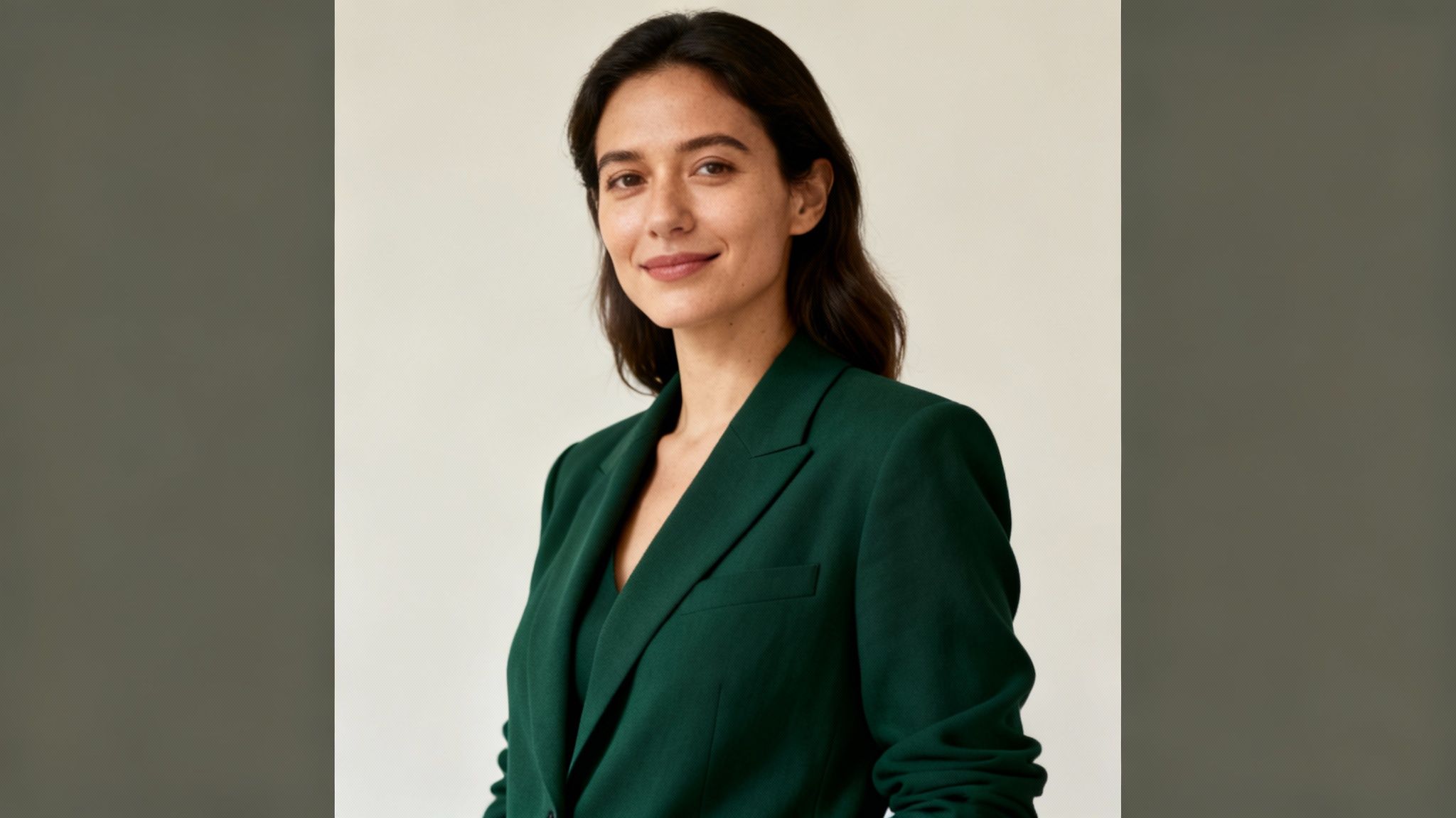 Professional woman wearing dark green blazer smiling confidently in studio portrait