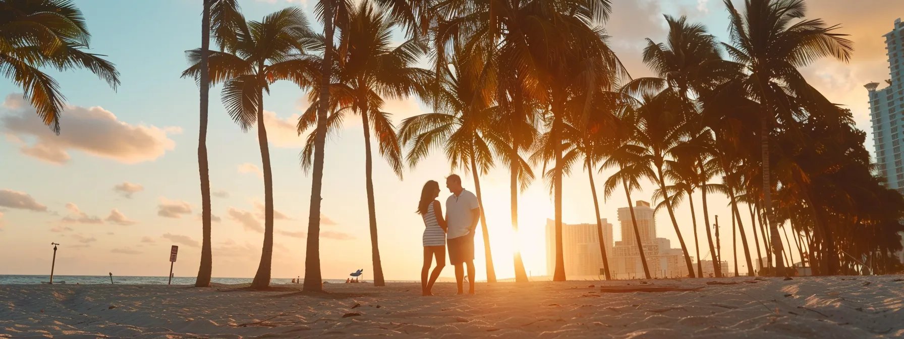 a couple standing on a sunlit miami beach, surrounded by palm trees, discussing photography details with a miami photographer.