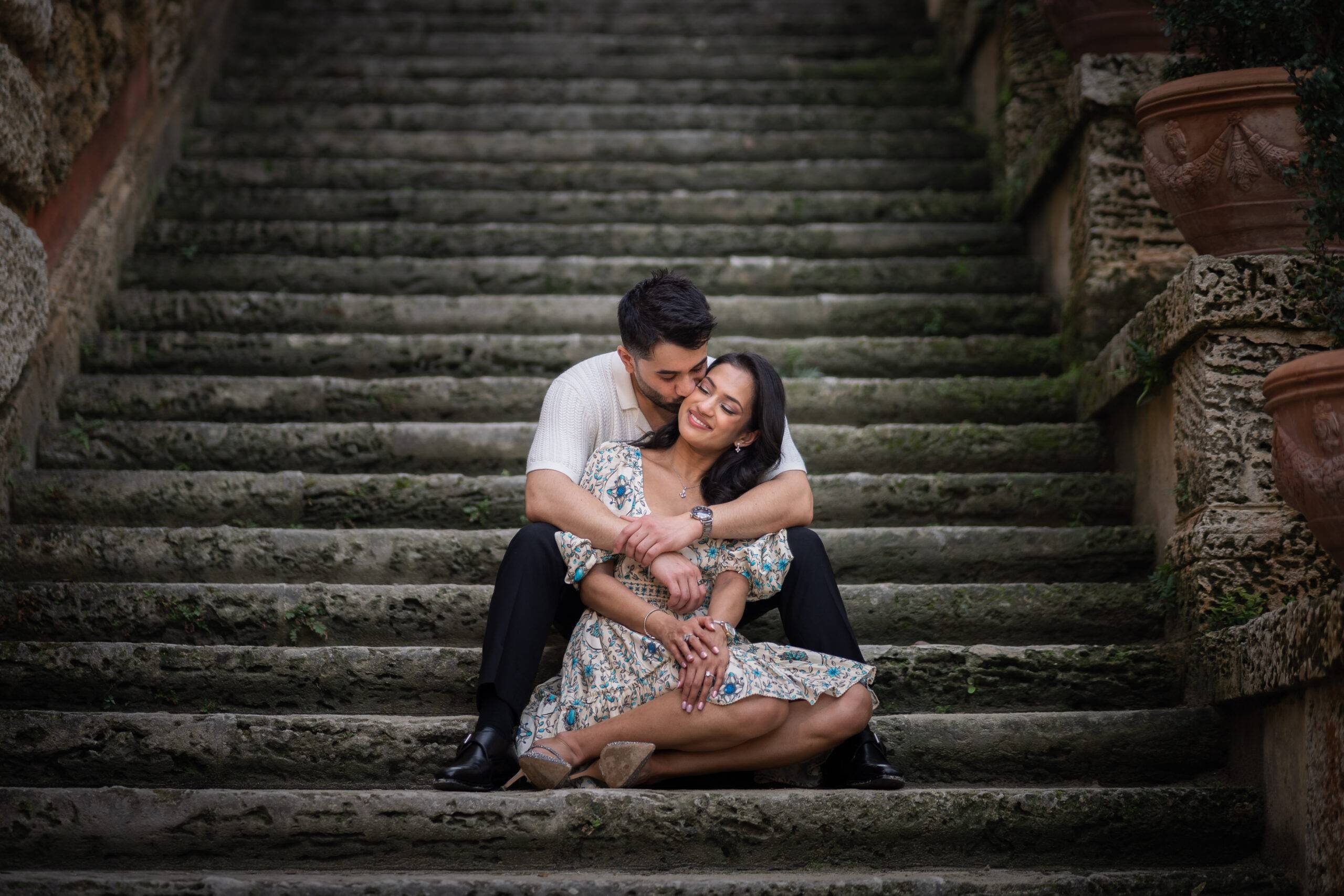 An engaged couple kissing on the stairs of Vizcaya gardens in Miami, FL