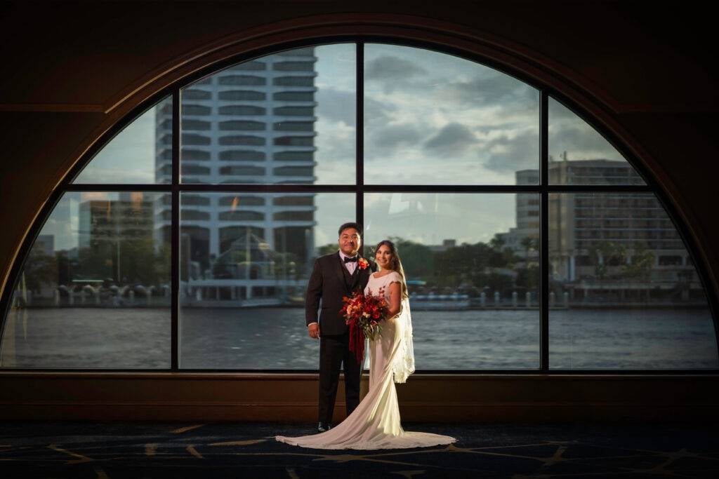 A bride and groom in front of a large bay window in Jacksonville, Florida.
